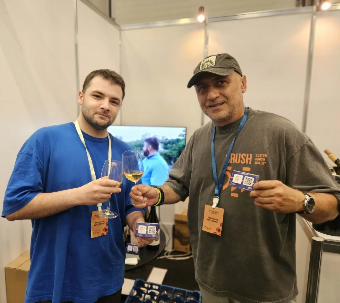 Two people toasting with wine at an expo, holding Dippi QR cards